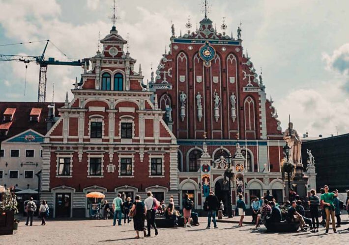 Picture of the House of the Blackheads in Riga, Latvia. It has a brownish facade with white details. It also has a blue clock and is decorated with four statues