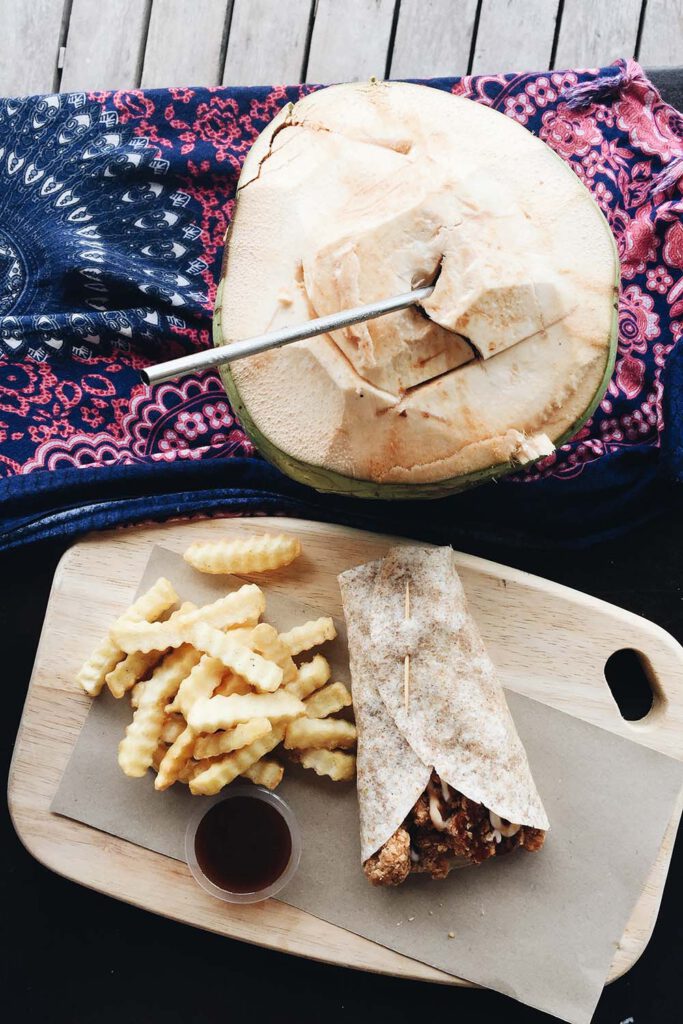 A coconut with a metal straw, along side with a burrito and fries