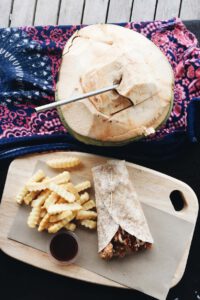A coconut with a metal straw, along side with a burrito and fries