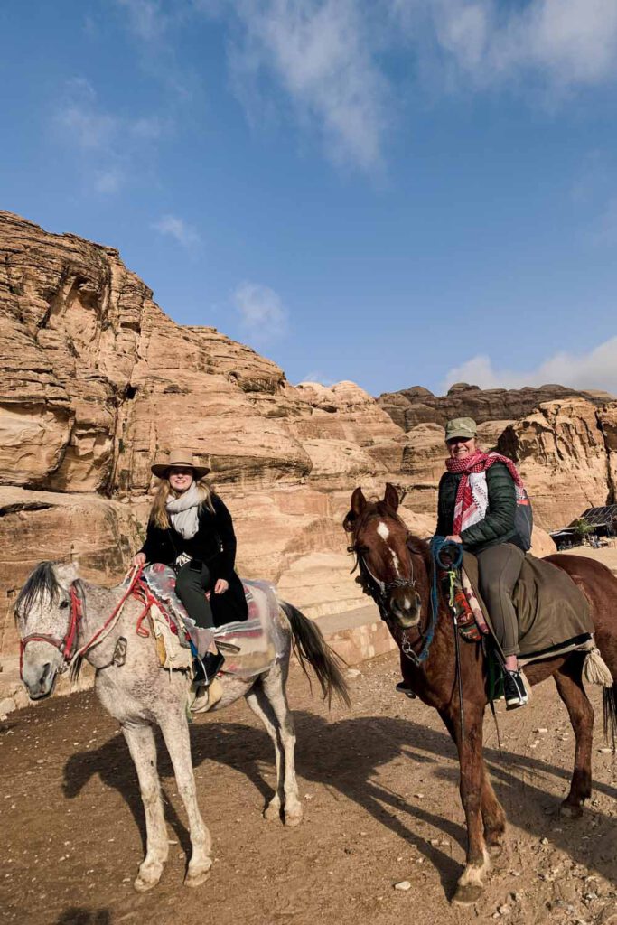 Women sitting on two horses, riding into Petra