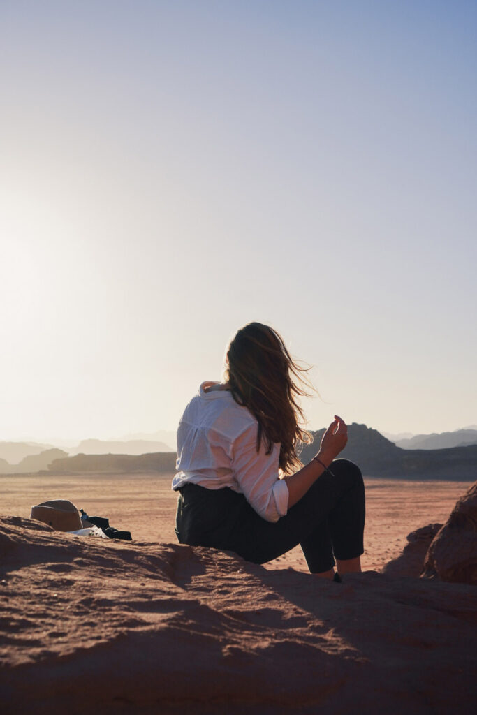 Girl sitting in front of the sunset in Wadi Rum Desert