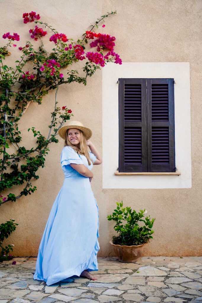 girl in a blue dreamy dress twirls in front of a terra cotta colored wall with pink flowers